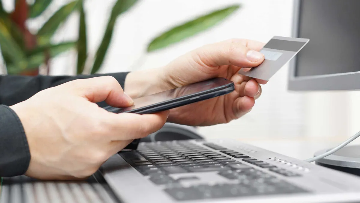 Zahlungsarten Headerbild Mann vor dem PC sitzend mit Mobiltelefon und Kreditkarte
