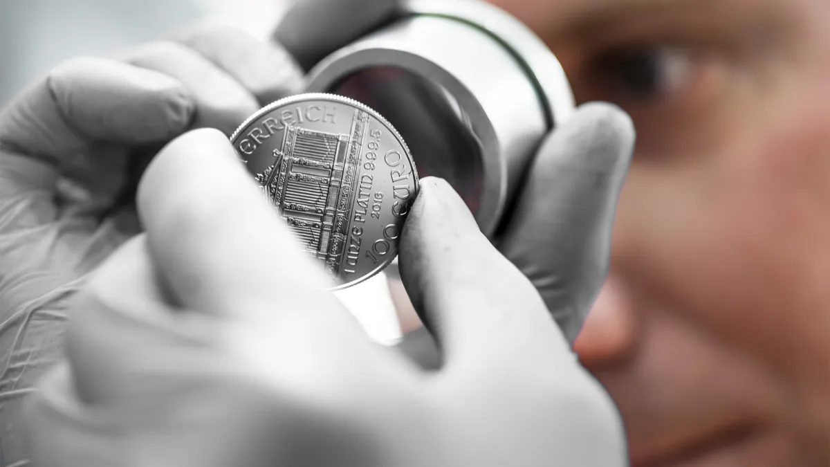 Platin Wiener Philharmoniker in Händen haltend mit Lupe und Gesicht